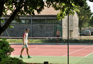 Deux personnes jouent au tennis sur un court extérieur à Flower Camping Le Bel Air en Nouvelle-Aquitaine, France.