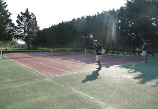 Folk spiller tennis på en udendørs bane omgivet af træer i Flower Camping Le Bel Air i Nouvelle-Aquitaine, Frankrig.