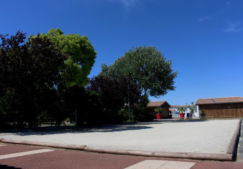 Foto van Flower Camping Le Bel Air met speelplaats, bomen en houten huisjes onder een heldere blauwe lucht.