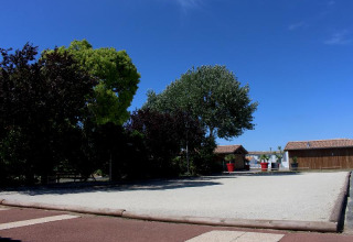 Foto van Flower Camping Le Bel Air met speelplaats, bomen en houten huisjes onder een heldere blauwe lucht.