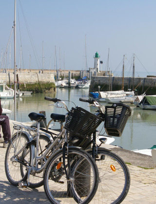Twee mensen zitten op een bankje bij de haven van La Flotte, Frankrijk, met fietsen en boten erbij.