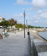 Boulevard aan zee in La Flotte, Nouvelle-Aquitaine, Frankrijk met cafés, bomen en aangemeerde boten.