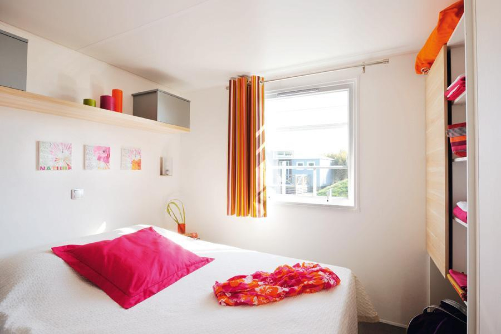 Lichte, compacte slaapkamer in een glampingaccommodatie met een gezellig bed en kleurrijke decoratie.