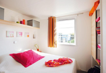 Chambre lumineuse et compacte dans un hébergement glamping avec lit douillet et déco colorée.