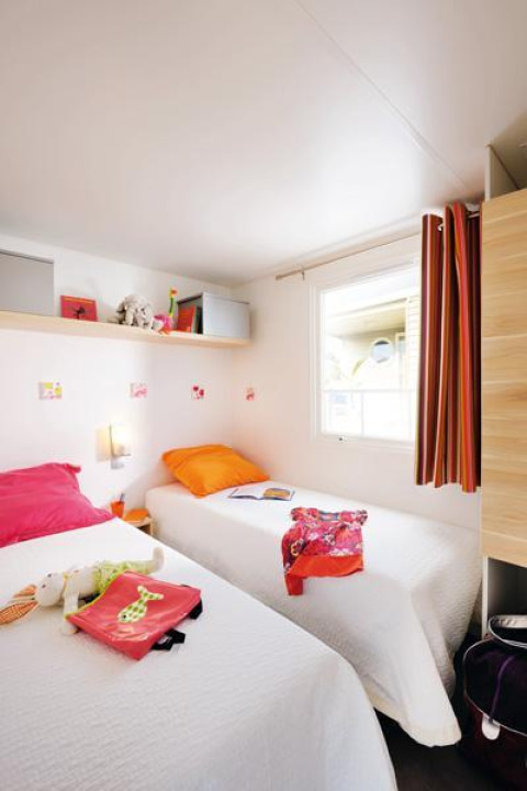 Lichte glampingkamer met twee eenpersoonsbedden, kleurrijke kussens, een raam en wanddecoratie.