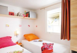 Chambre de glamping lumineuse avec deux lits simples, coussins colorés, fenêtre et décorations murales.