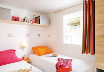 Chambre de glamping lumineuse avec deux lits simples, coussins colorés, fenêtre et décorations murales.