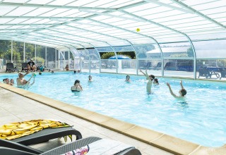 Overdækket swimmingpool med familier, børn og voksne der nyder ferien på Flower Camping Le Kerleyou i Bretagne.