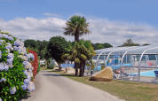 Hyggelig feriepark i Bretagne, Frankrig, med overdækket pool, palmer og blomstrende hække.