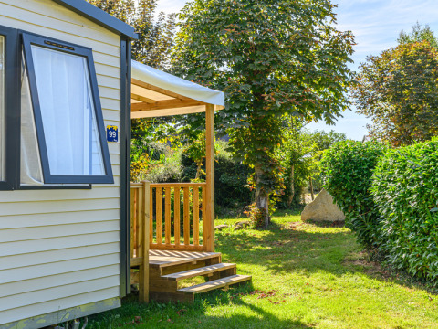 Sunny mobile home with wooden terrace and lush garden at Flower Camping Le Kerleyou, Brittany, France.