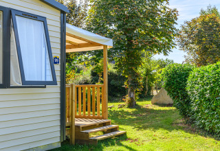Solrigt billede af mobilhome med træterrasse og grøn have på Flower Camping Le Kerleyou i Bretagne, Frankrig.
