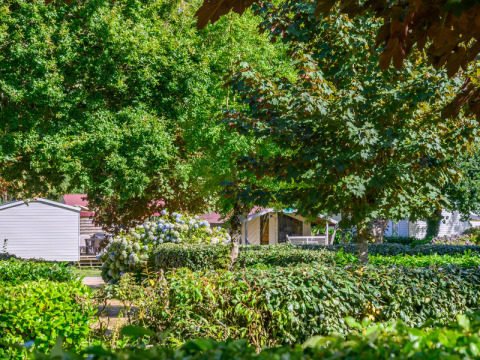 Árboles y setos verdes rodean casas móviles en Flower Camping Le Kerleyou, parque de vacaciones en Bretaña, Francia.