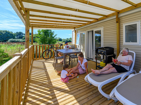 Familia relajándose en una terraza de madera cubierta en Flower Camping Le Kerleyou, Bretaña, Francia.
