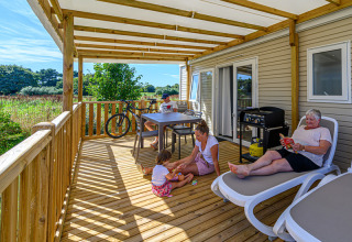Familia relajándose en una terraza de madera cubierta en Flower Camping Le Kerleyou, Bretaña, Francia.
