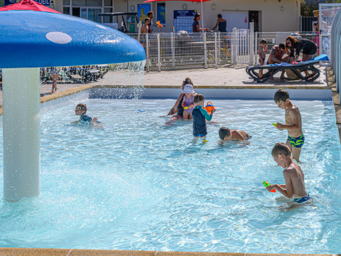 Children play in a splash pool with a mushroom fountain at Flower Camping Le Kerleyou in Brittany, France.