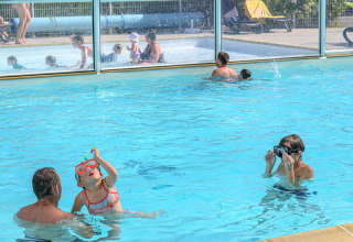 Famiglie si divertono in piscina coperta al Flower Camping Le Kerleyou, un villaggio vacanze in Bretagna, Francia.