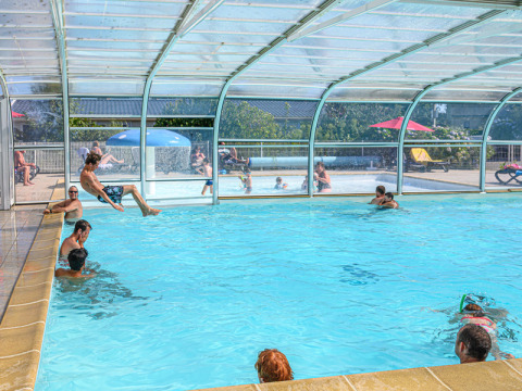 Piscina cubierta en Flower Camping Le Kerleyou con personas nadando y jugando en el agua en Bretaña, Francia.