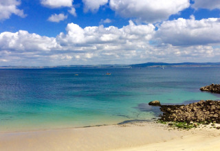 Impresionante vista de playa de arena y mar azul en Flower Camping Le Kerleyou en Bretaña, Francia.