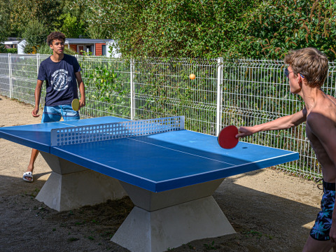 Twee jonge mannen spelen buitentafeltennis bij Flower Camping Le Kerleyou, een vakantiepark in Bretagne, Frankrijk.