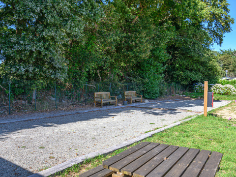 Area relax con panche e sentiero ghiaioso accanto agli alberi verdi al Flower Camping Le Kerleyou, Bretagna.