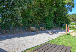 Zona de descanso con bancos y sendero de grava junto a árboles verdes en Flower Camping Le Kerleyou, Bretaña.