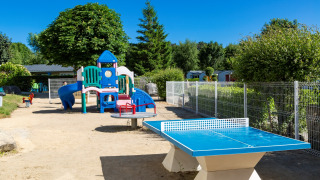 Speeltuin en blauwe tafeltennistafel bij Flower Camping Le Kerleyou in Bretagne, Frankrijk op een zonnige dag.