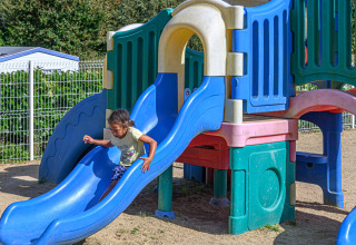 Een kind speelt op een blauwe glijbaan op de speeltuin van Flower Camping Le Kerleyou in Bretagne, Frankrijk.