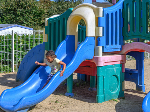 Un enfant joue sur un toboggan bleu dans l’aire de jeux du Flower Camping Le Kerleyou en Bretagne, France.