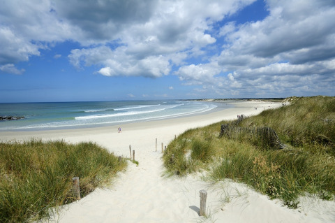 Sandy beach with grassy dunes and ocean waves at Flower Camping Le Kerleyou in Brittany, France, on a cloudy day.