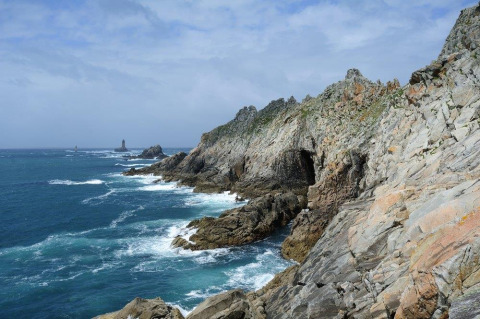 Rocky coastline with blue sea and waves near Flower Camping Le Kerleyou holiday park in Brittany, France.