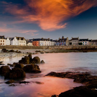 Kustzicht bij Douarnenez, Bretagne, Frankrijk, met kleurrijke huizen, rotsachtige kust en fraaie zonsondergang.