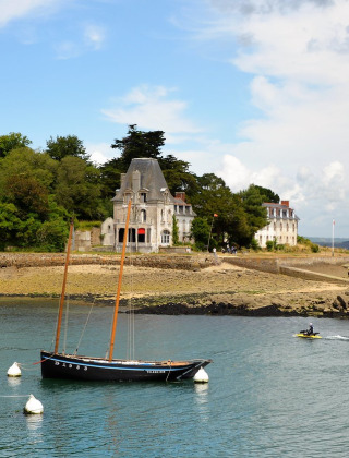 Uitzicht op Douarnenez in Bretagne, Frankrijk, met zeilboten en statige villa’s langs een beboste kustlijn.