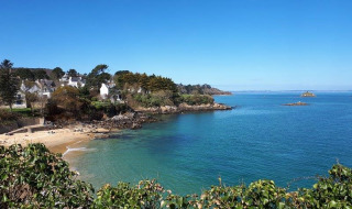 Kustlandschap nabij Douarnenez, Bretagne, Frankrijk, met blauwe zee, groen struikgewas en witte huizen.