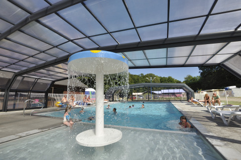 Covered swimming pool with water feature and guests relaxing at Flower Camping La Chênaie in Normandy, France.