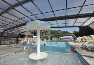 Piscina cubierta con fuente de agua y huéspedes relajándose en Flower Camping La Chênaie en Normandía, Francia.