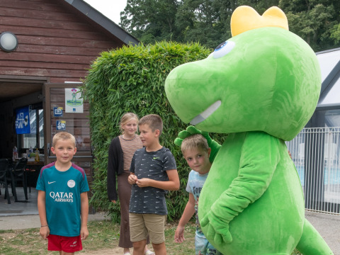 Des enfants posent avec une grande mascotte verte à Flower Camping La Chênaie, un parc de vacances en Normandie.