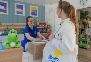 Receptionist byder gæst velkommen i Flower Camping La Chênaie i Normandiet, Frankrig, med venligt smil.