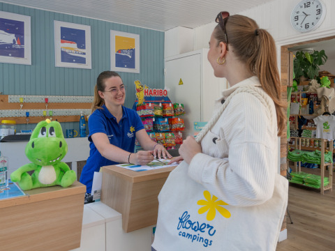 Receptionist welcomes guest with a smile at Flower Camping La Chênaie holiday park in Normandy, France.