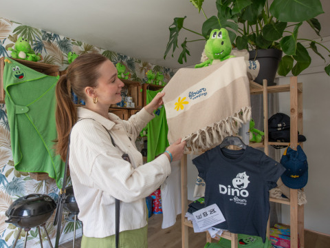 Vrouw bekijkt dinosaurusthema souvenirs in een shop bij Flower Camping La Chênaie, Normandië, Frankrijk.