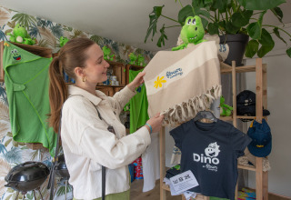 Frau betrachtet Souvenirs mit grünem Dino in einem Geschäft im Flower Camping La Chênaie in der Normandie.