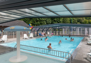 Piscina cubierta con huéspedes nadando y tumbonas en Flower Camping La Chênaie en Normandía, Francia.