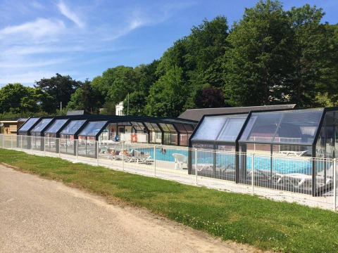 Covered outdoor swimming pool at Flower Camping La Chênaie in Normandy, France, with loungers and green trees.