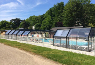 Covered outdoor swimming pool at Flower Camping La Chênaie in Normandy, France, with loungers and green trees.