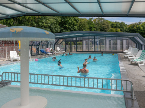 Überdachtes Schwimmbad mit spielenden und schwimmenden Menschen im Flower Camping La Chênaie in der Normandie.