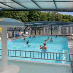 Covered swimming pool with people enjoying the water at Flower Camping La Chênaie holiday park in Normandy, France.