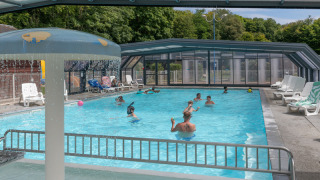 Covered swimming pool with people enjoying the water at Flower Camping La Chênaie holiday park in Normandy, France.