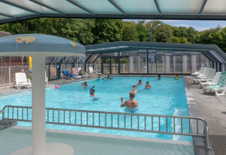 Überdachtes Schwimmbad mit spielenden und schwimmenden Menschen im Flower Camping La Chênaie in der Normandie.