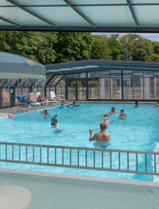 Overdekt zwembad met mensen die zwemmen en spelen bij Flower Camping La Chênaie vakantiepark in Normandië.