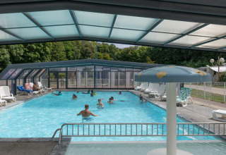 Überdachtes Schwimmbad mit spielenden Menschen und Liegestühlen im Flower Camping La Chênaie, Normandie, Frankreich.