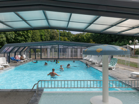 Covered swimming pool with people swimming and lounging at Flower Camping La Chênaie, Normandy, France.